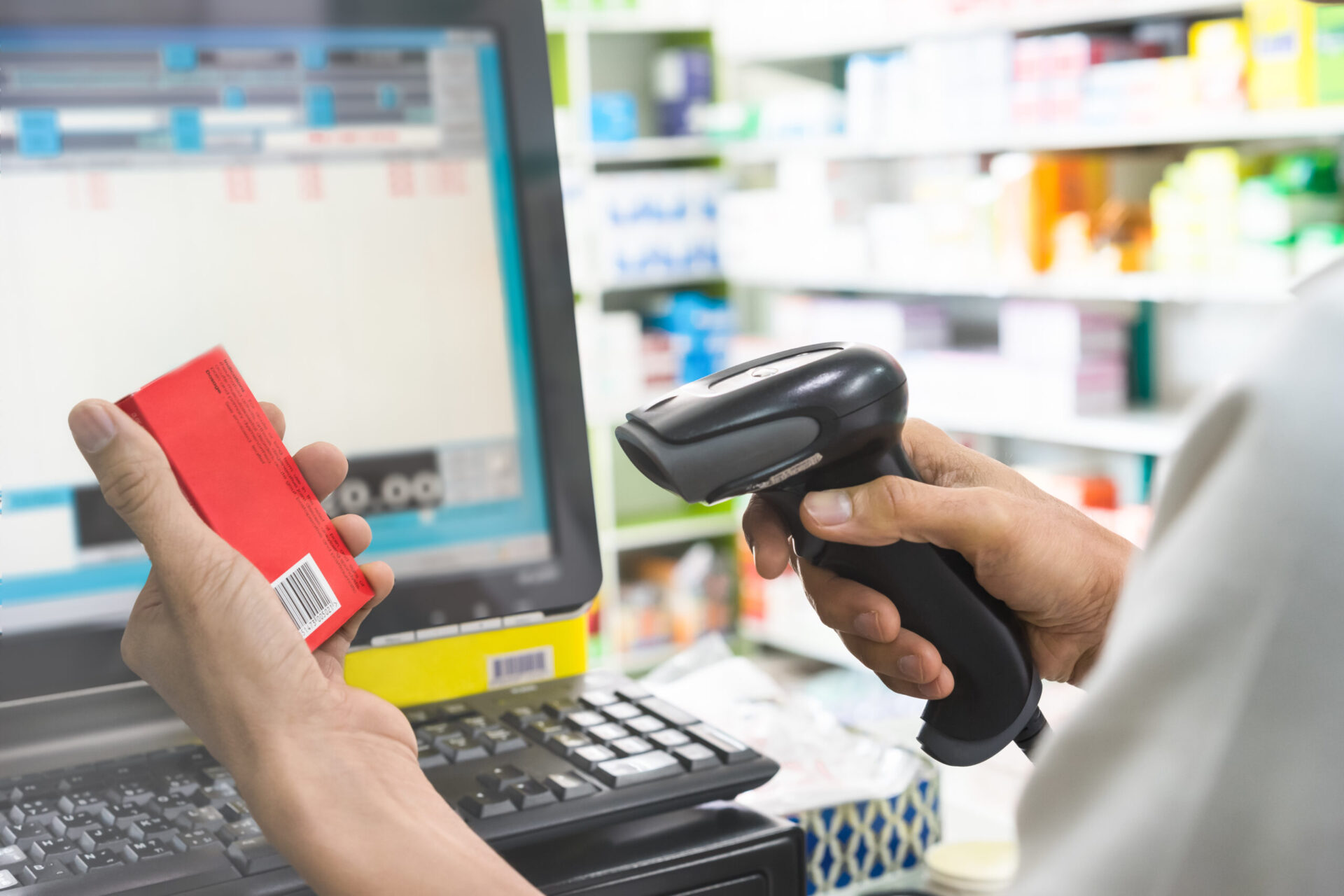 Pharmacist scanning price on a red medicine box with barcode reader in pharmacy store
