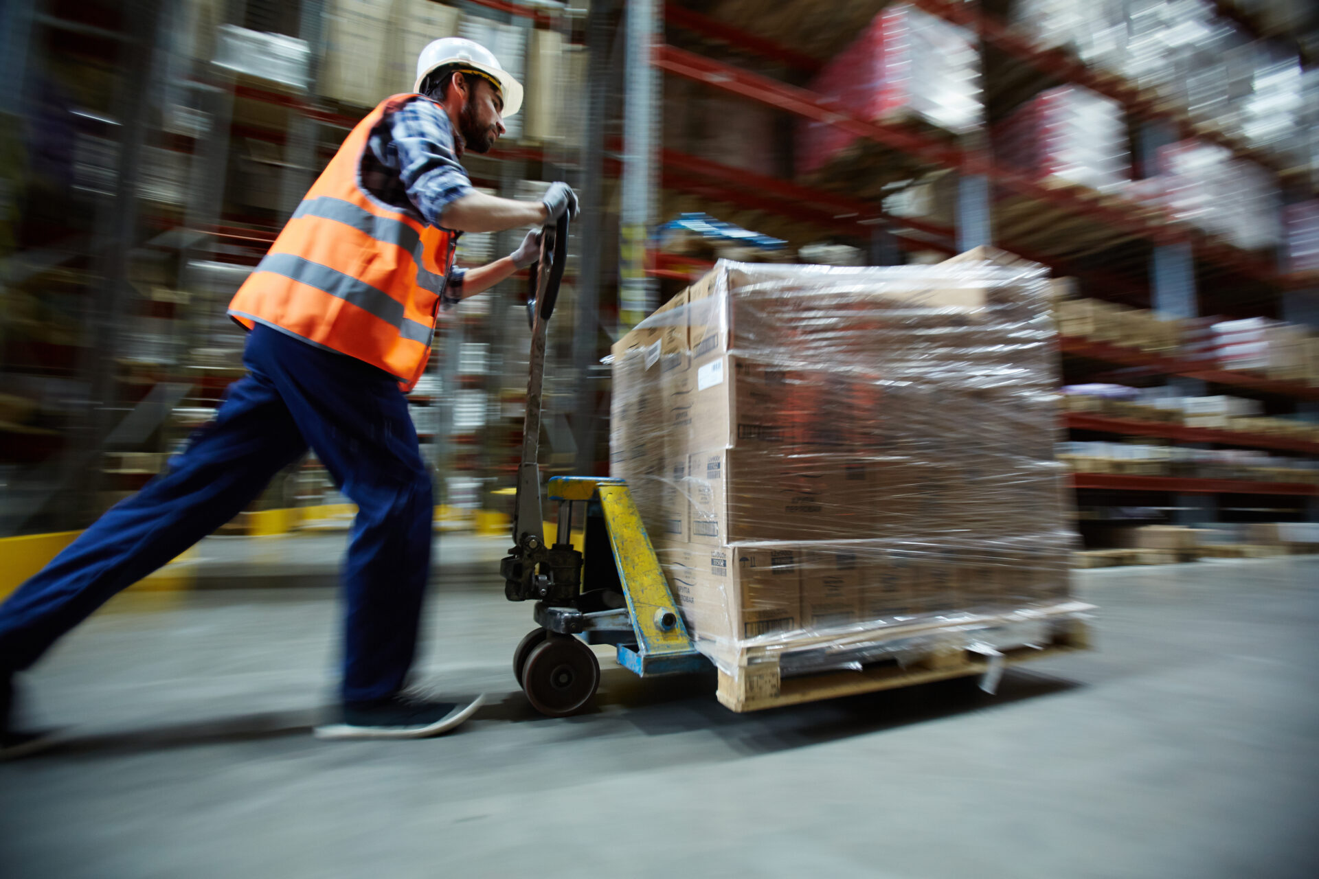 Man in hard hart pushing a pallet on a cart through a warehouse