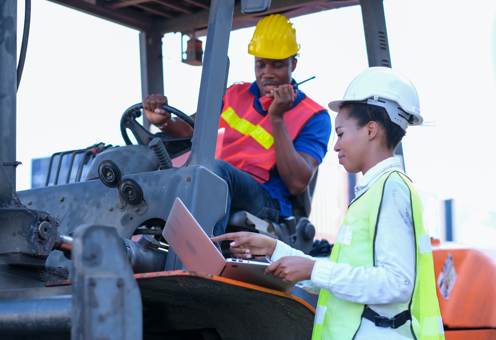 Woman on laptop talking to forklift operator 
